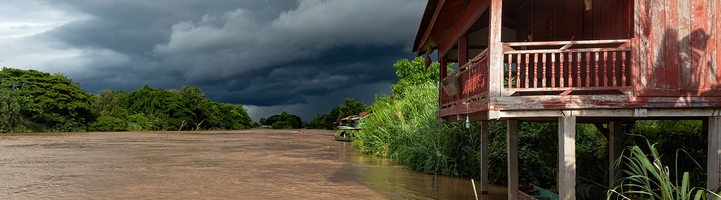 Mekong bank with wooden dwelling on stilts under grey stormy clouds at golden hour, in Don Det, Si Phan Don, Laos.